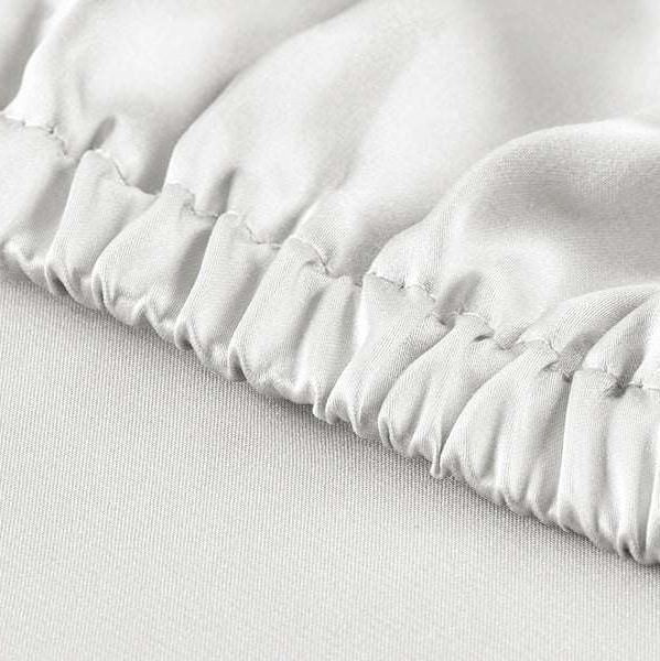 White Close-up view of the elastic hem on a powder white silk fitted sheet, ensuring a snug fit for the mattress.