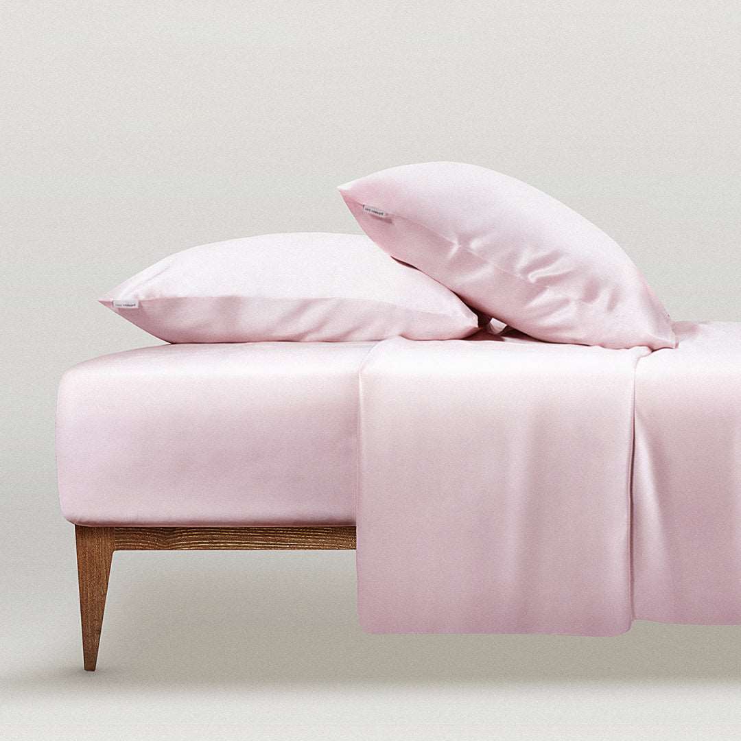 Pink Blush pink silk pillowcase set on a bed by Dariia Day, offering a luxurious and smooth sleeping experience.