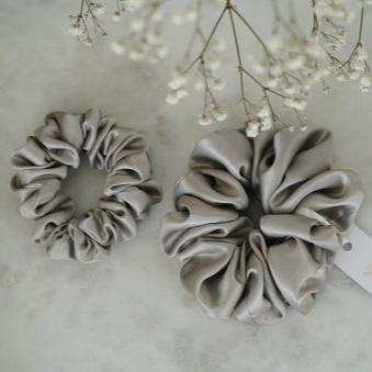 Grey Set of two grey silk scrunchies by Dariia Day, shown on a marble surface, perfect for maintaining hair health and style.