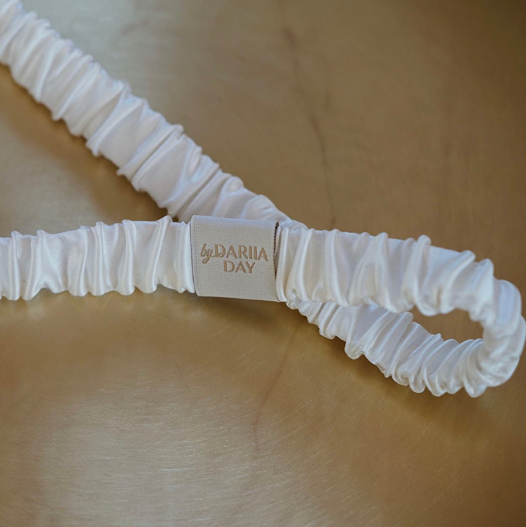 White Close-up of by Dariia Day Powder White Silk Headband on a gold surface.