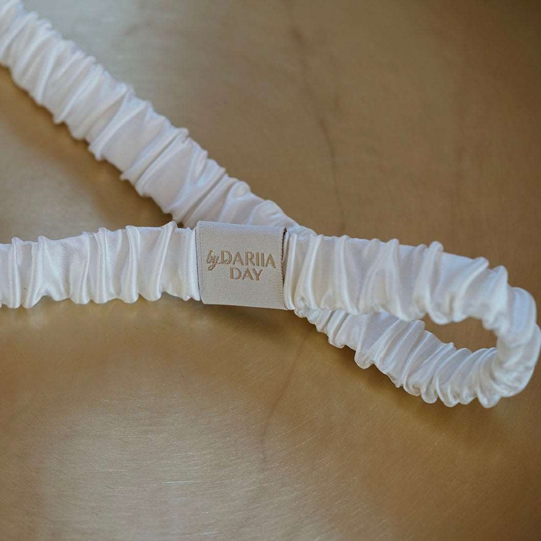 White Close-up of by Dariia Day Powder White Silk Headband on a gold surface.