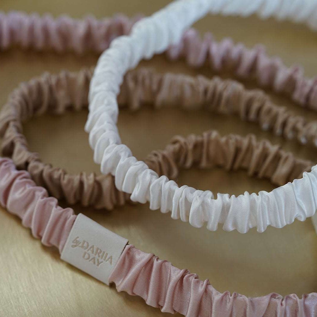 Pink A collection of luxurious silk headbands in blush pink, white, and beige, by Dariia Day, displayed on a golden tray