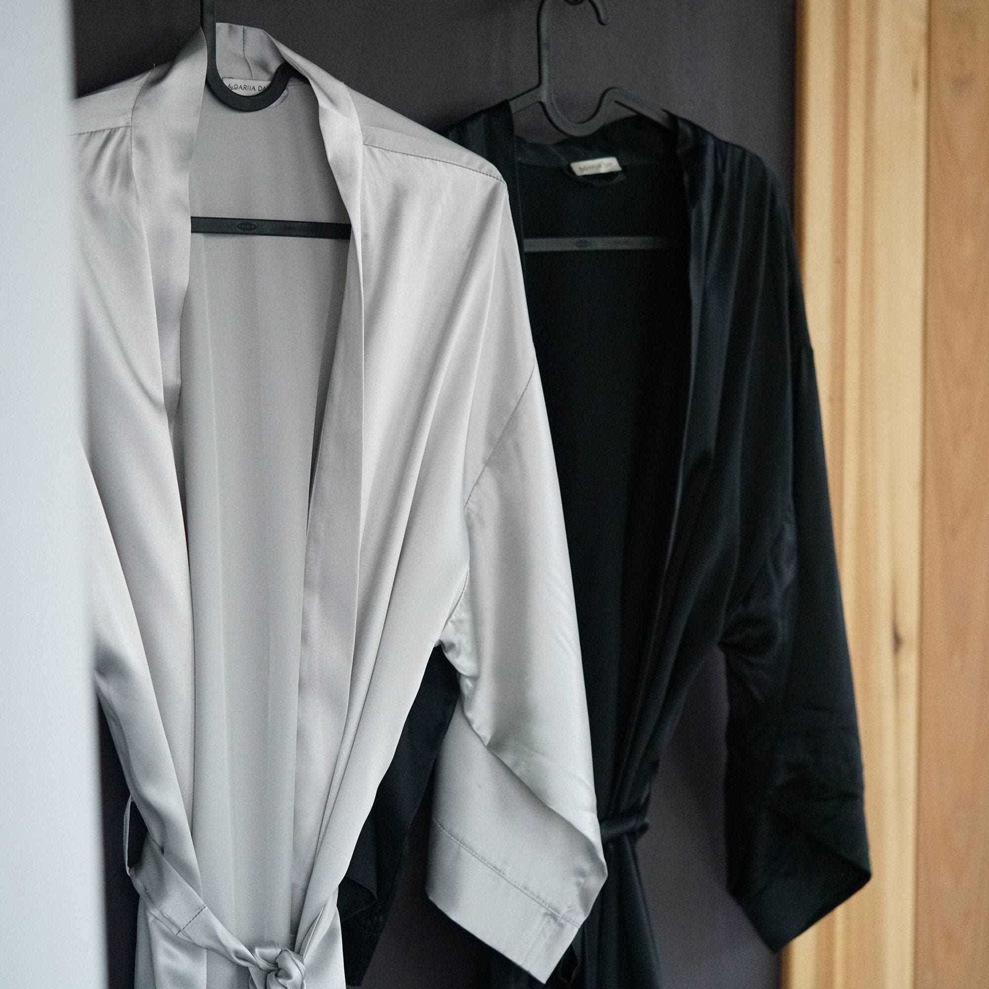 Black Two silk robes, one black and one silver, hanging on hooks against a dark wall.