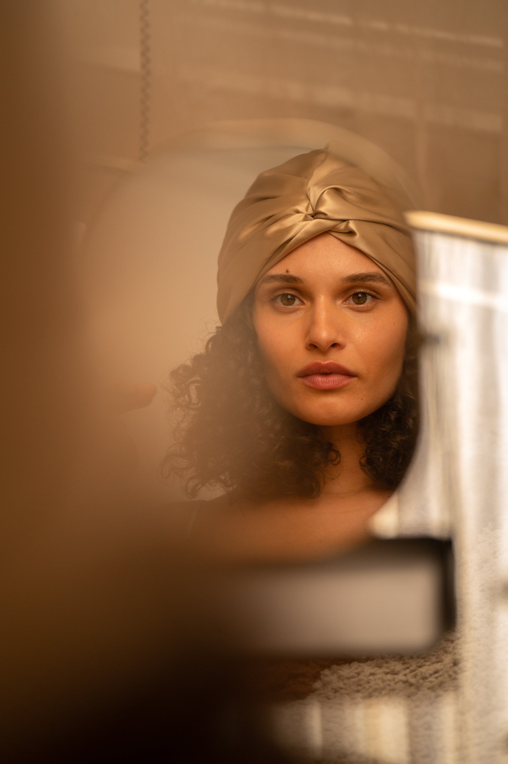 Beige Woman wearing a gold turban in front of a mirror beige