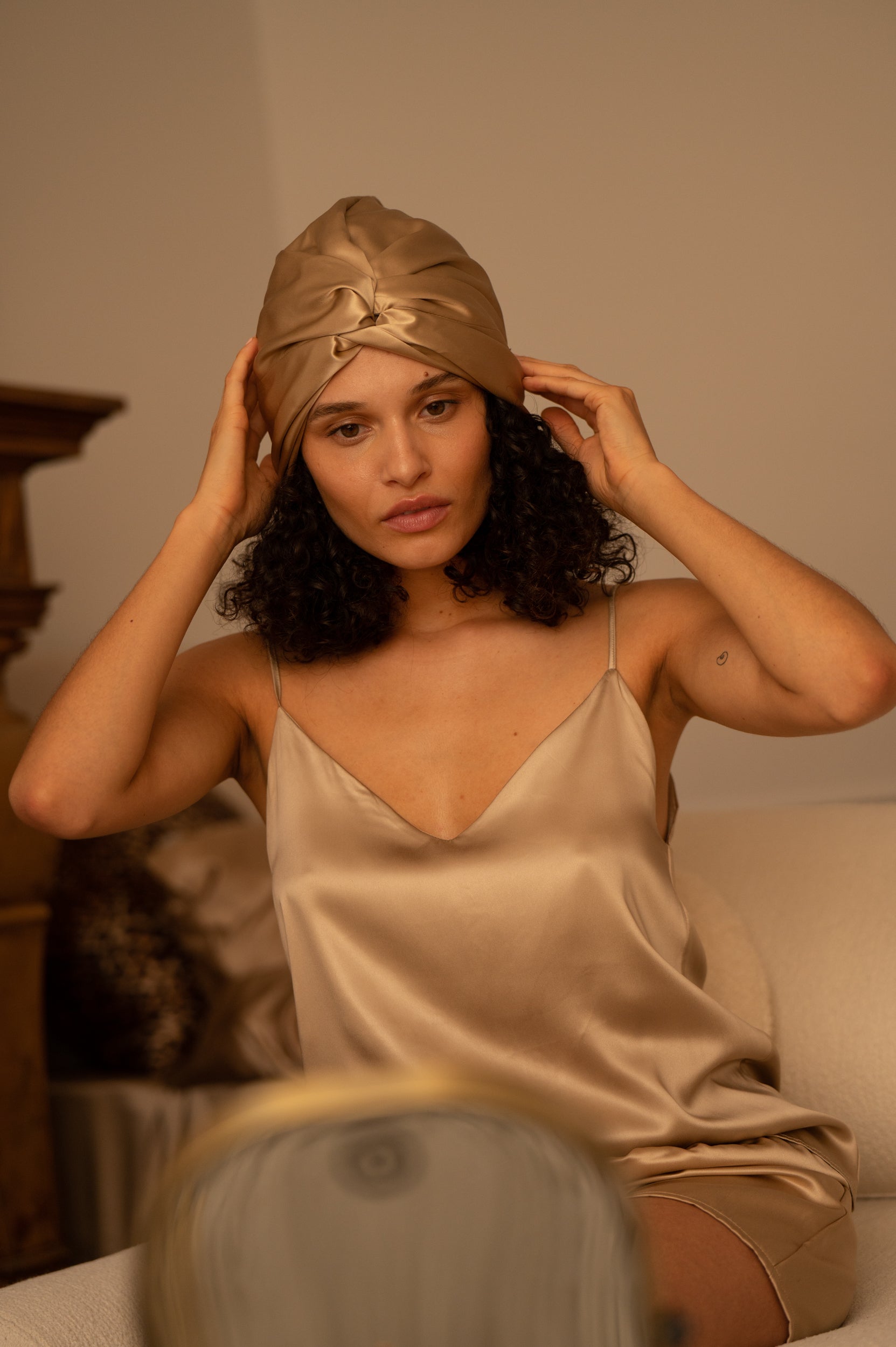 Beige Woman wearing a beige silk turban and nightgown, sitting on a bed