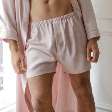 Pink Man standing near a window wearing blush pink silk boxers and a matching silk robe by Dariia Day.