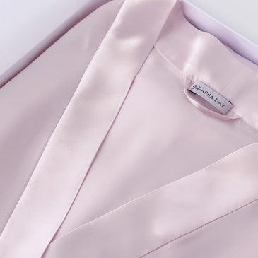 Pink Close-up of a light pink silk robe by Dariia Day, showcasing smooth fabric and brand label.
