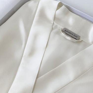 White Detailed close-up of a powder white silk robe by Dariia Day, folded in a box, highlighting the fabric texture and branding.