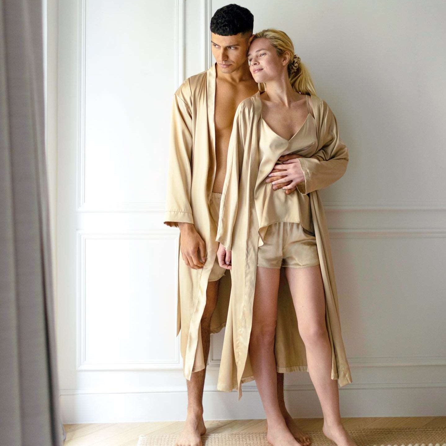 Beige Couple standing in beige silk robes by Dariia Day, with the man leaning against the wall and the woman embracing him.