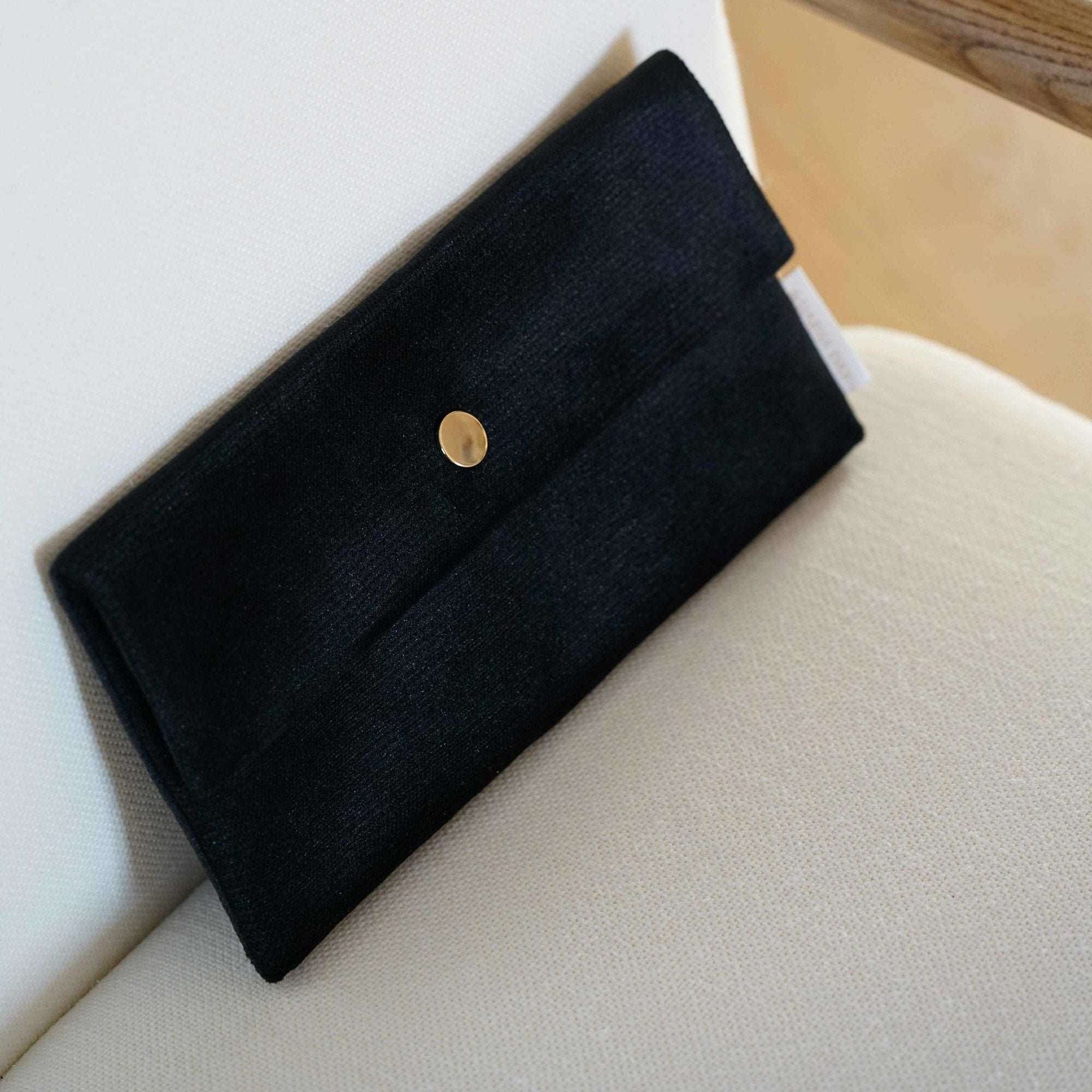 Black Dariia Day Midnight Black Velvet Pouch placed elegantly on a beige chair.