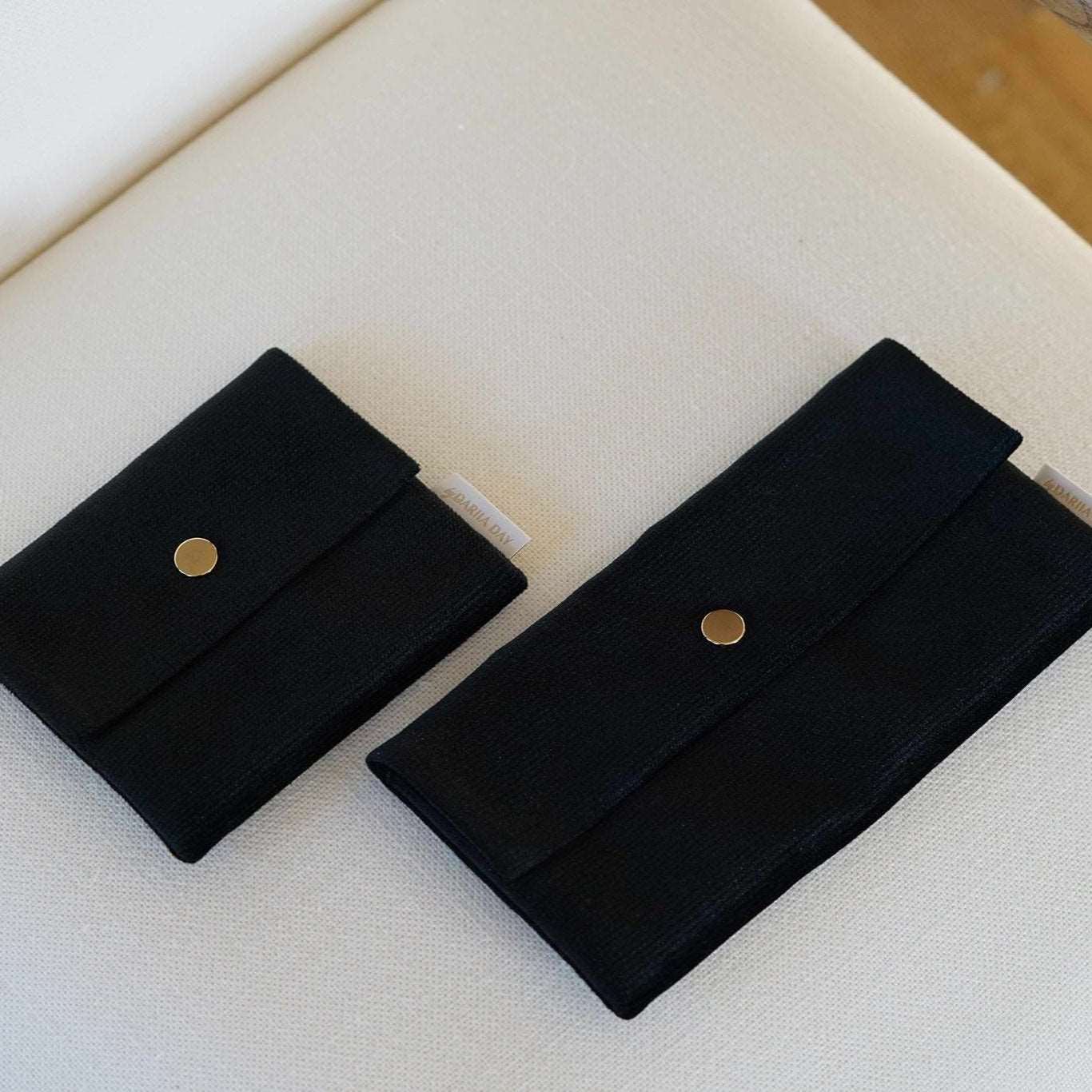 Black Two sizes of Dariia Day Midnight Black Velvet Pouch laid flat on a beige fabric surface.