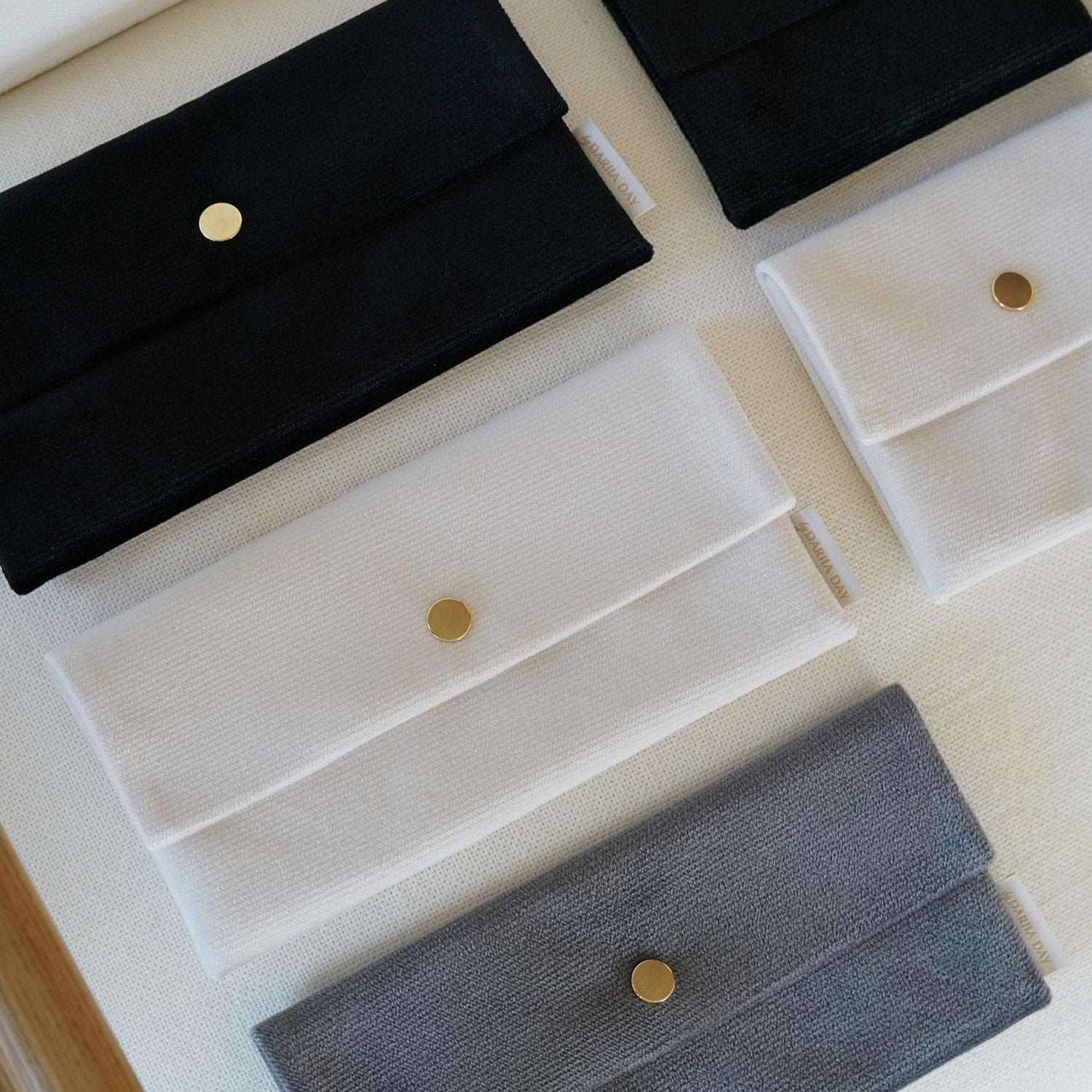 Vanilla Dariia Day Velvet Pouch collection in Midnight Black, Powder White, and Silver Grey displayed on a beige surface.