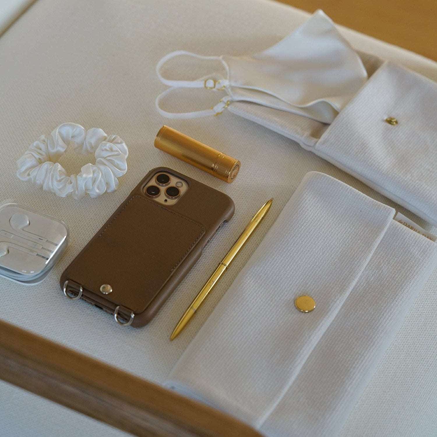 Vanilla Flatlay of Dariia Day White Vanilla Pouch with accessories, including a scrunchie, mask, phone, and gold lipstick.