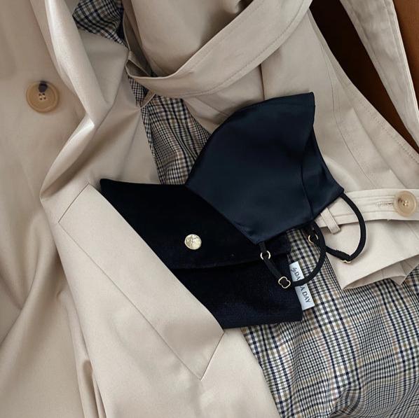 Black Midnight black silk face mask and pouch resting on a beige trench coat with a plaid lining, by Daria Day.