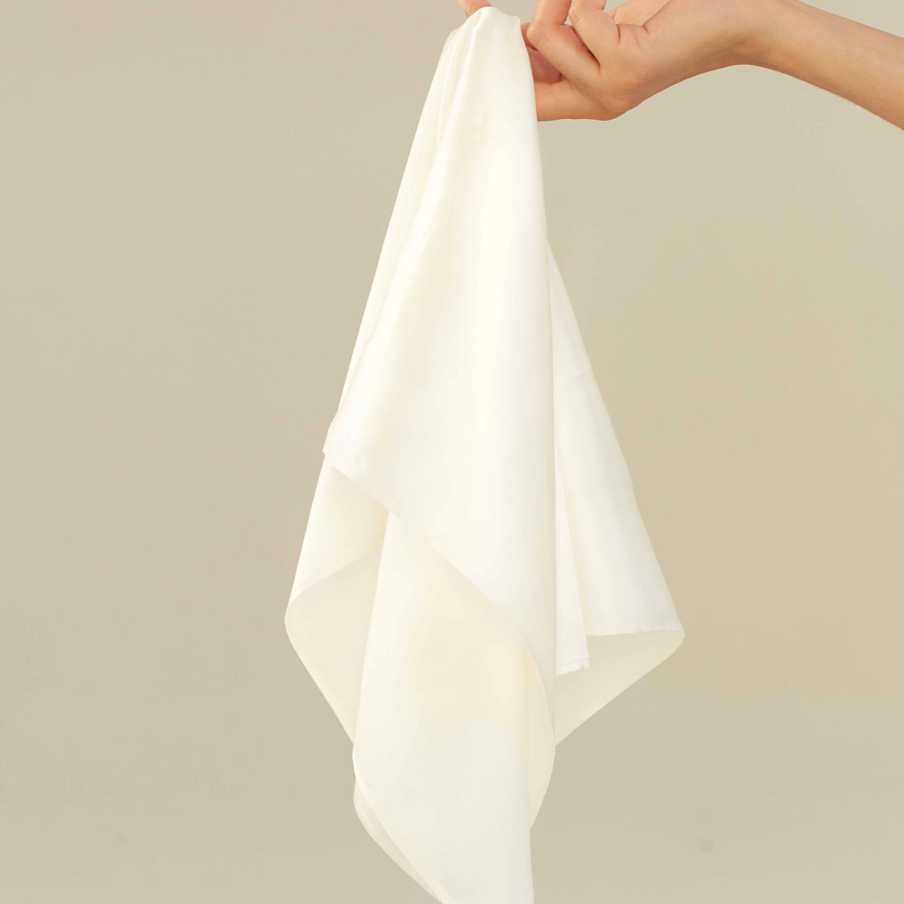 White A hand holding a powder white silk scarf by Dariia Day, showcasing its soft and luxurious fabric