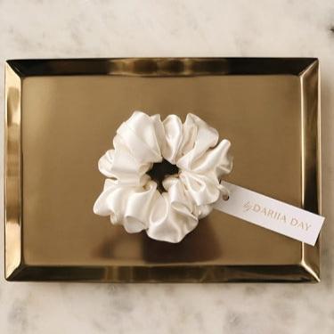 White Powder white silk scrunchie by Dariia Day resting on a gold tray, a perfect luxury accessory for hair care.