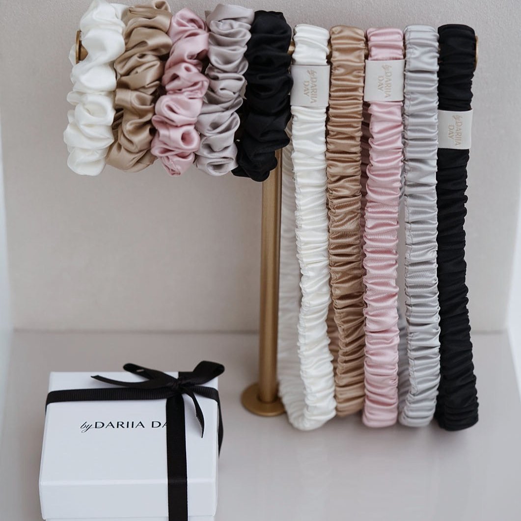 Beige Silk scrunchies and headbands collection by Dariia Day in various colors displayed on a stand.