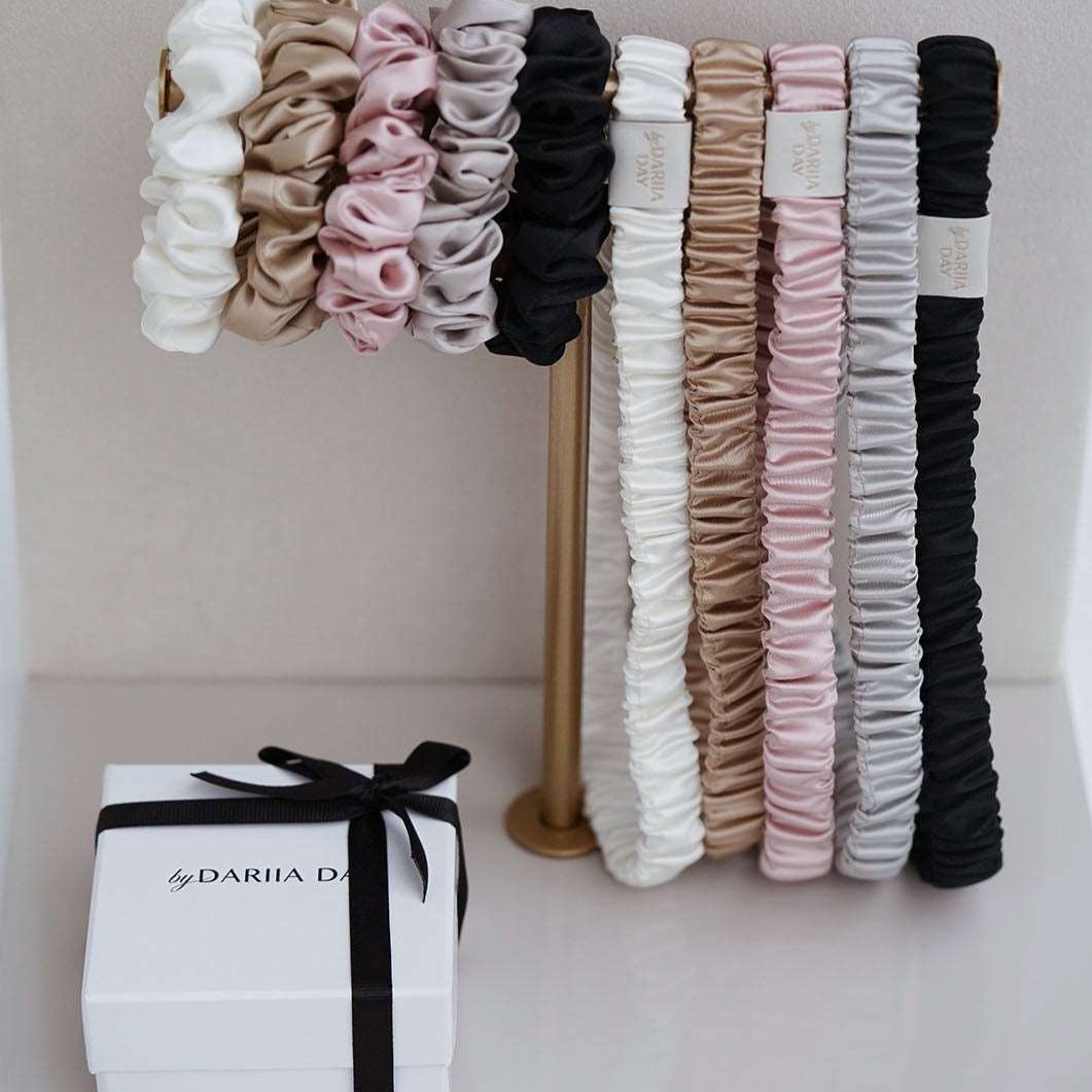 Black Silk scrunchies and headbands collection by Dariia Day in various colors displayed on a stand.
