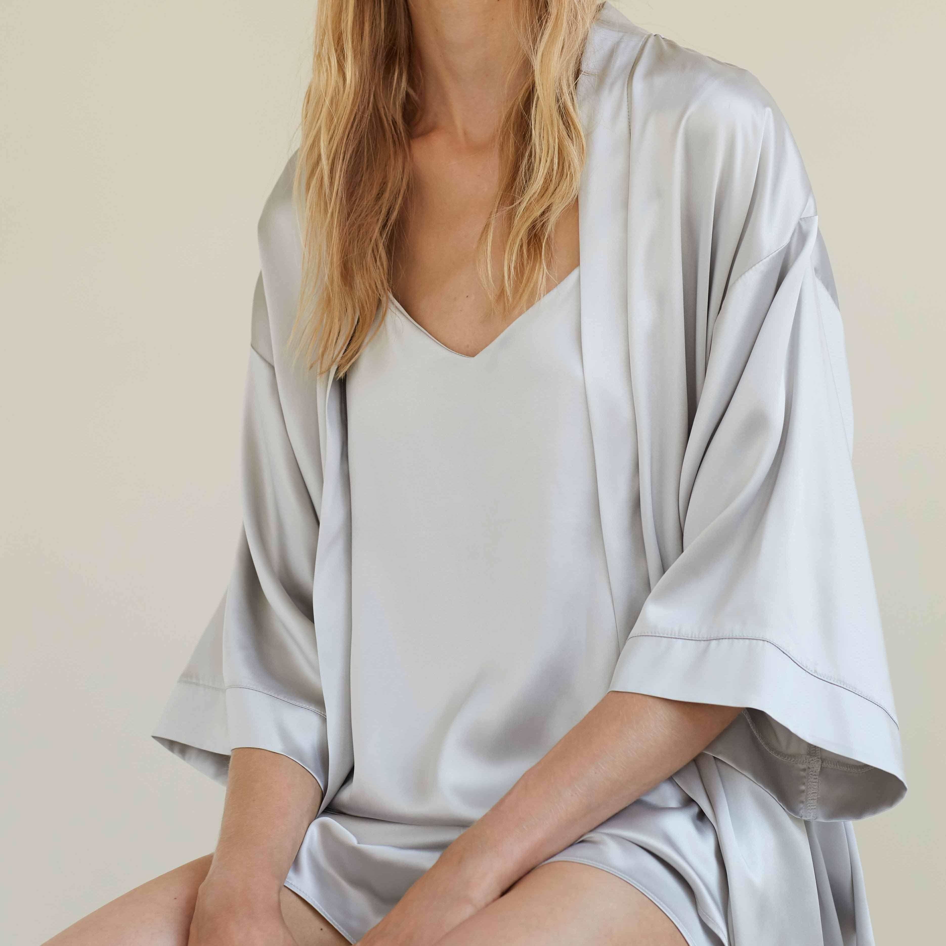 Grey Woman sitting in a silver grey silk robe and camisole set by Dariia Day, enjoying the soft and luxurious fabric.