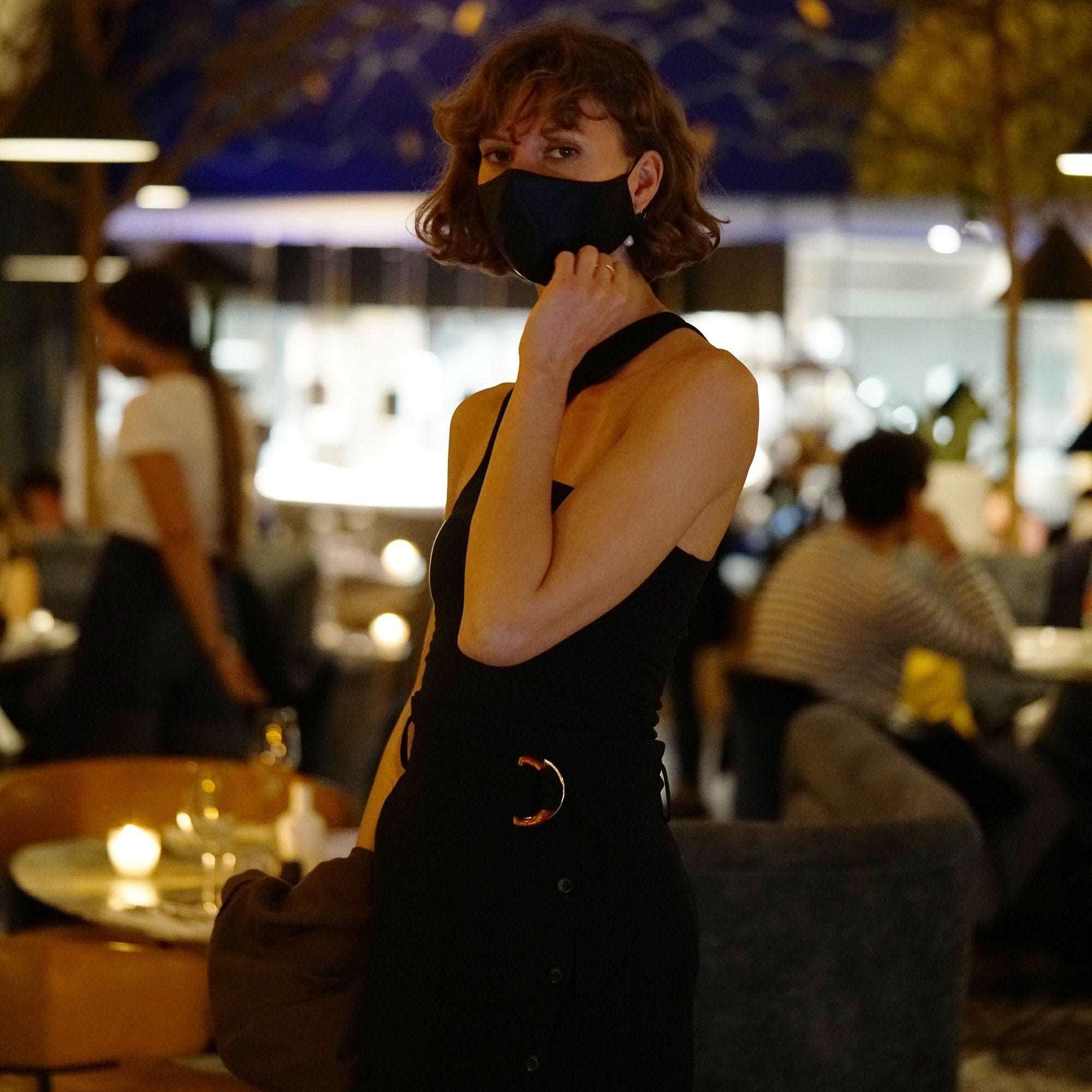 Black Woman wearing a midnight black silk face mask by Dariia Day in an elegant restaurant.