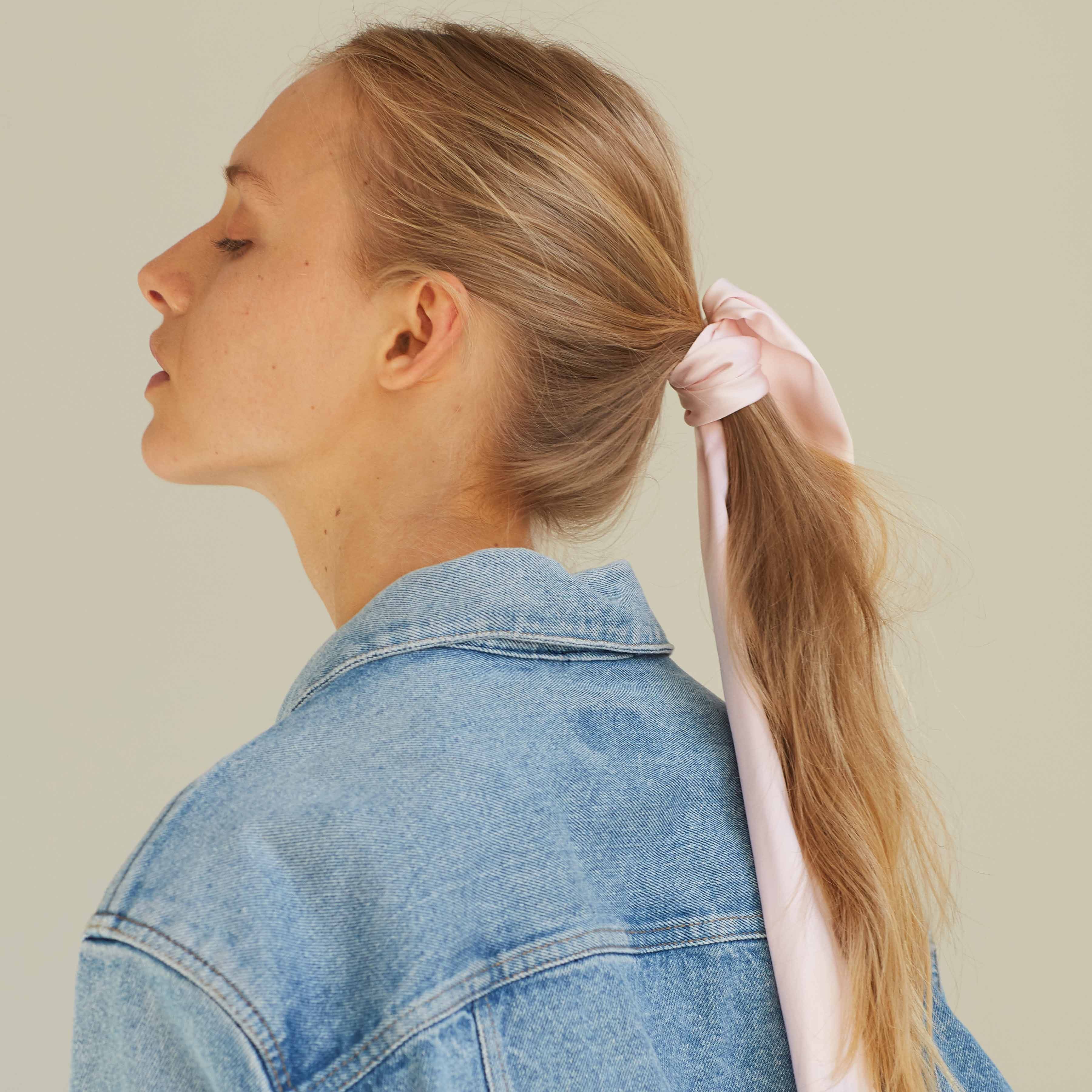 Back view of blush pink silk scarf tied around a ponytail, paired with a denim jacket, by Dariia Day.