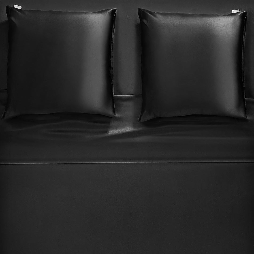 A pair of black silk pillowcases arranged on a matching black silk bedspread, creating a luxurious and elegant look.