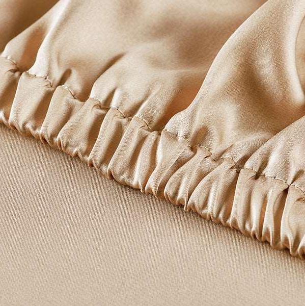 Detailed view of the high-quality craftsmanship of a French beige silk fitted sheet with an elastic hem, providing a secure and snug fit for any mattress.