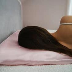 Woman enjoying a restful sleep on a luxurious pink silk pillowcase and sleep mask set by Dariia Day.