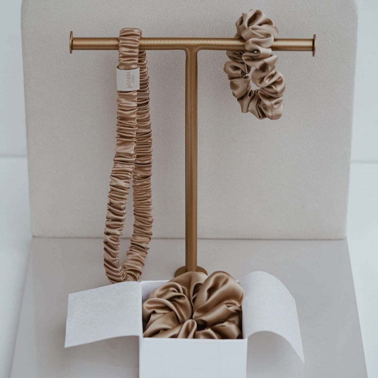 A chic display featuring a beige silk scrunchie and headband from by Dariia Day, set against an elegant backdrop.