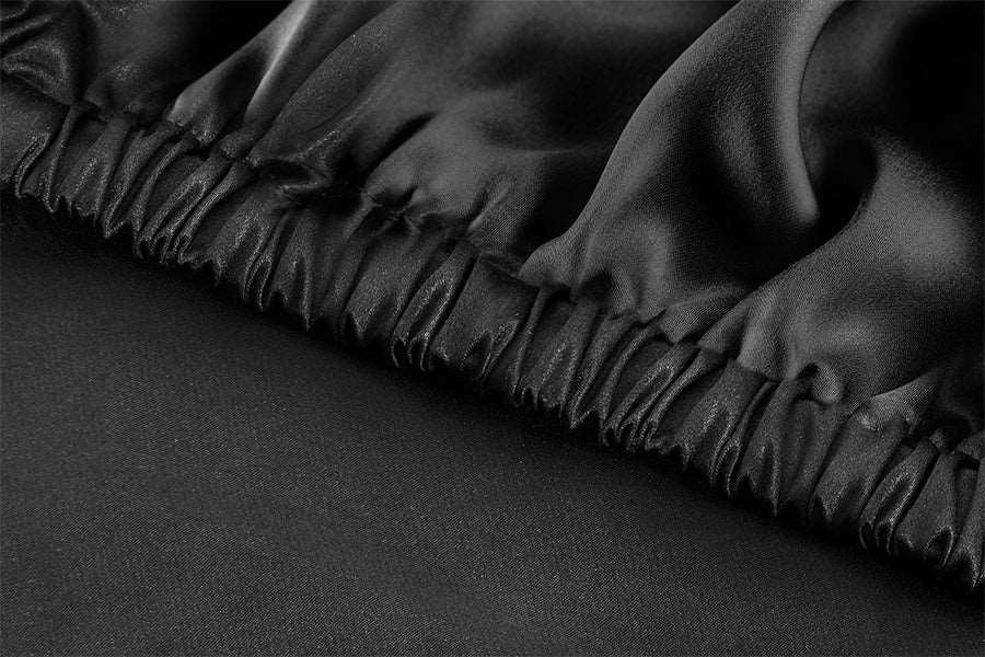 Detailed shot of the elastic band on a silk fitted sheet in Midnight Black, highlighting the secure fit and quality finish.