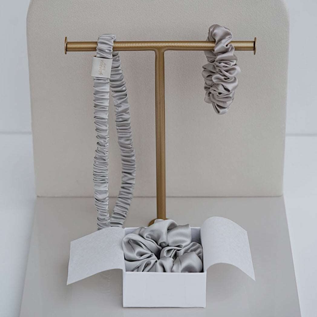 Set of two grey silk scrunchies by Dariia Day, shown on a marble surface, perfect for maintaining hair health and style.