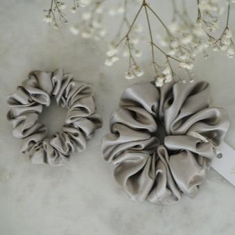 Set of two grey silk scrunchies by Dariia Day, shown on a marble surface, perfect for maintaining hair health and style.