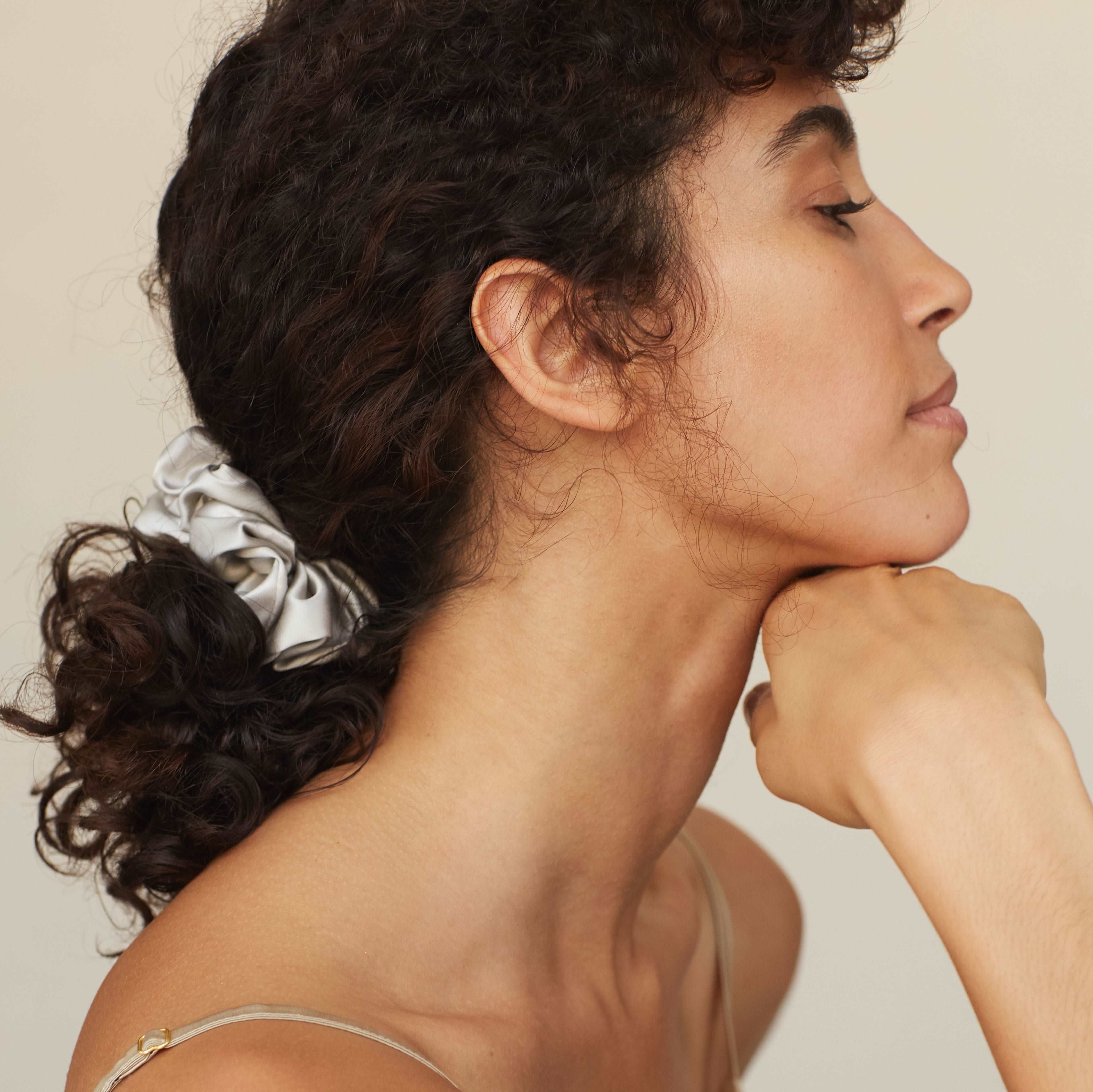 Model wearing a grey silk scrunchie by Dariia Day, highlighting the soft, luxurious texture in naturally curly hair.