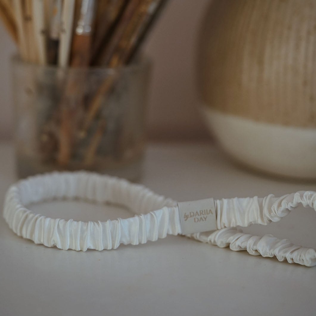 by Dariia Day Powder White Silk Headband placed elegantly with art brushes in the background, crafted from smooth mulberry silk.