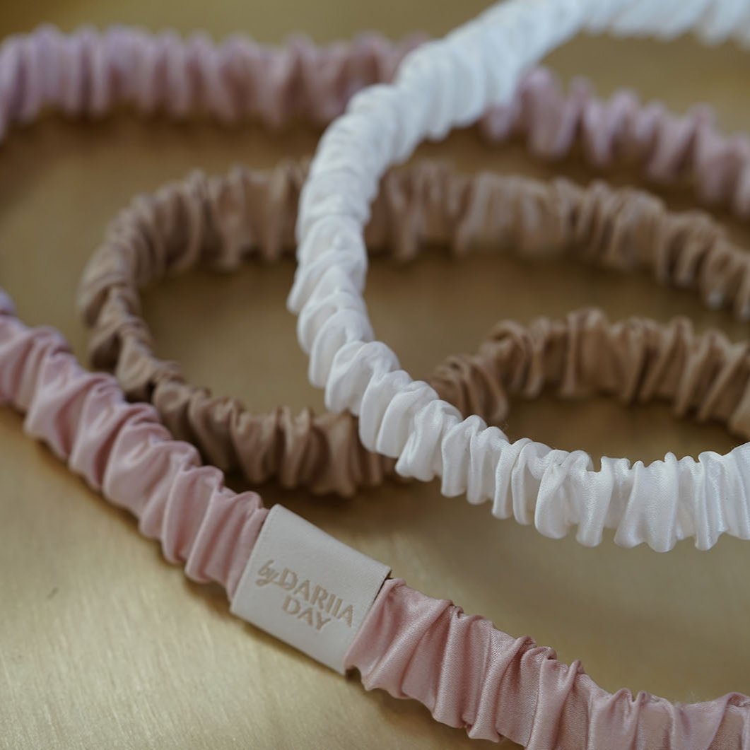 A collection of luxurious silk headbands in blush pink, white, and beige, by Dariia Day, displayed on a golden tray