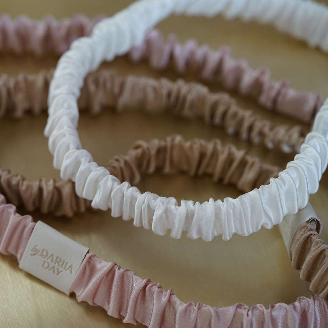 A collection of luxurious silk headbands in blush pink, white, and beige, by Dariia Day, displayed on a golden tray