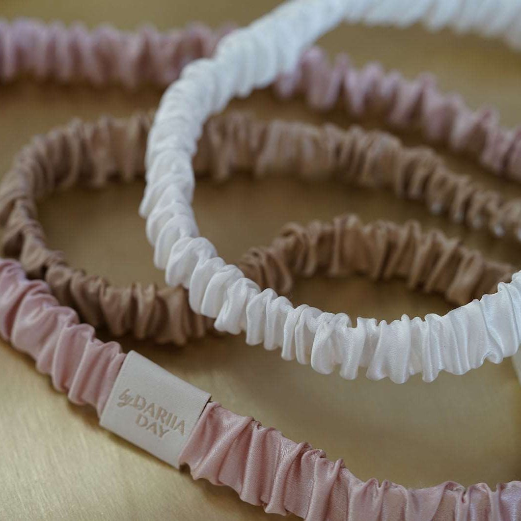 A collection of luxurious silk headbands in blush pink, white, and beige, by Dariia Day, displayed on a golden tray