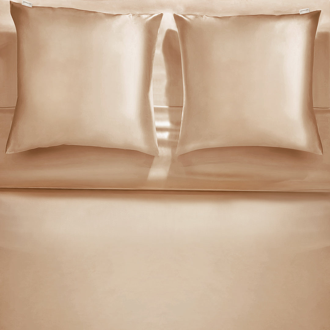 Beige silk pillowcase with a matching silk eye mask by Dariia Day, placed on a white pillow.