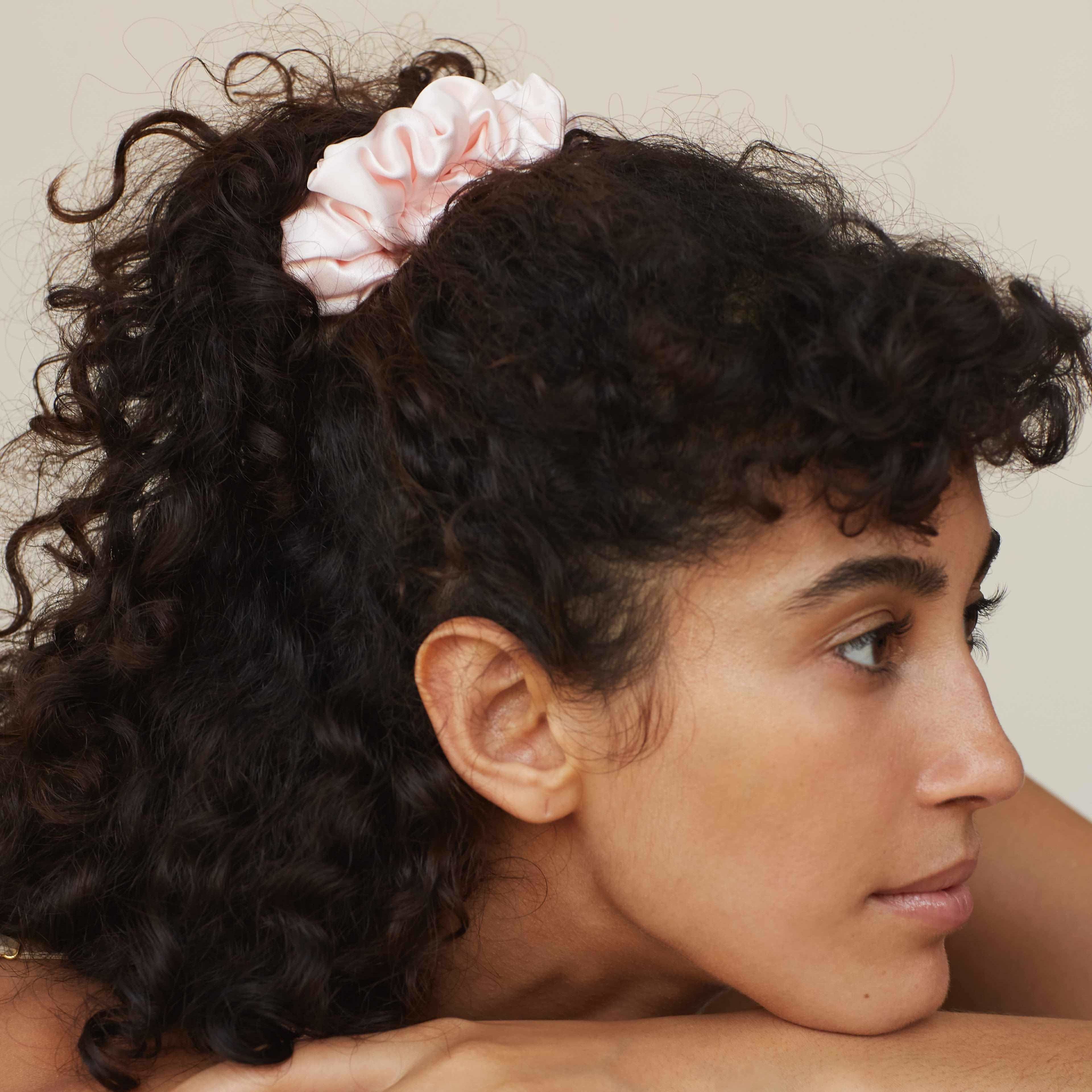 Pink Close-up of a woman with curly hair, wearing a blush pink silk scrunchie by Dariia Day