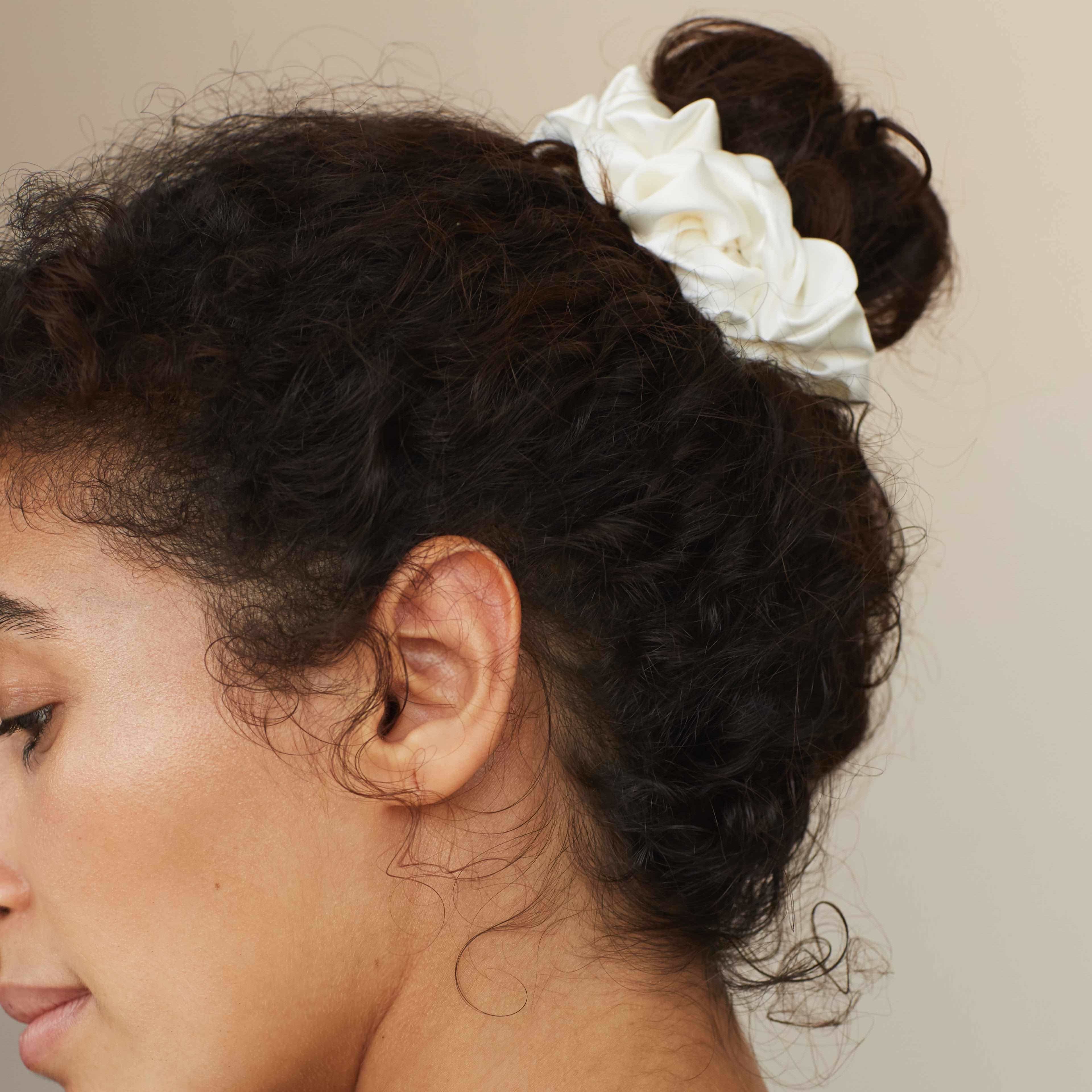 Side profile of a woman wearing by Dariia Day Powder White Silk Scrunchie in her curly hair, showcasing the smooth texture of mulberry silk.