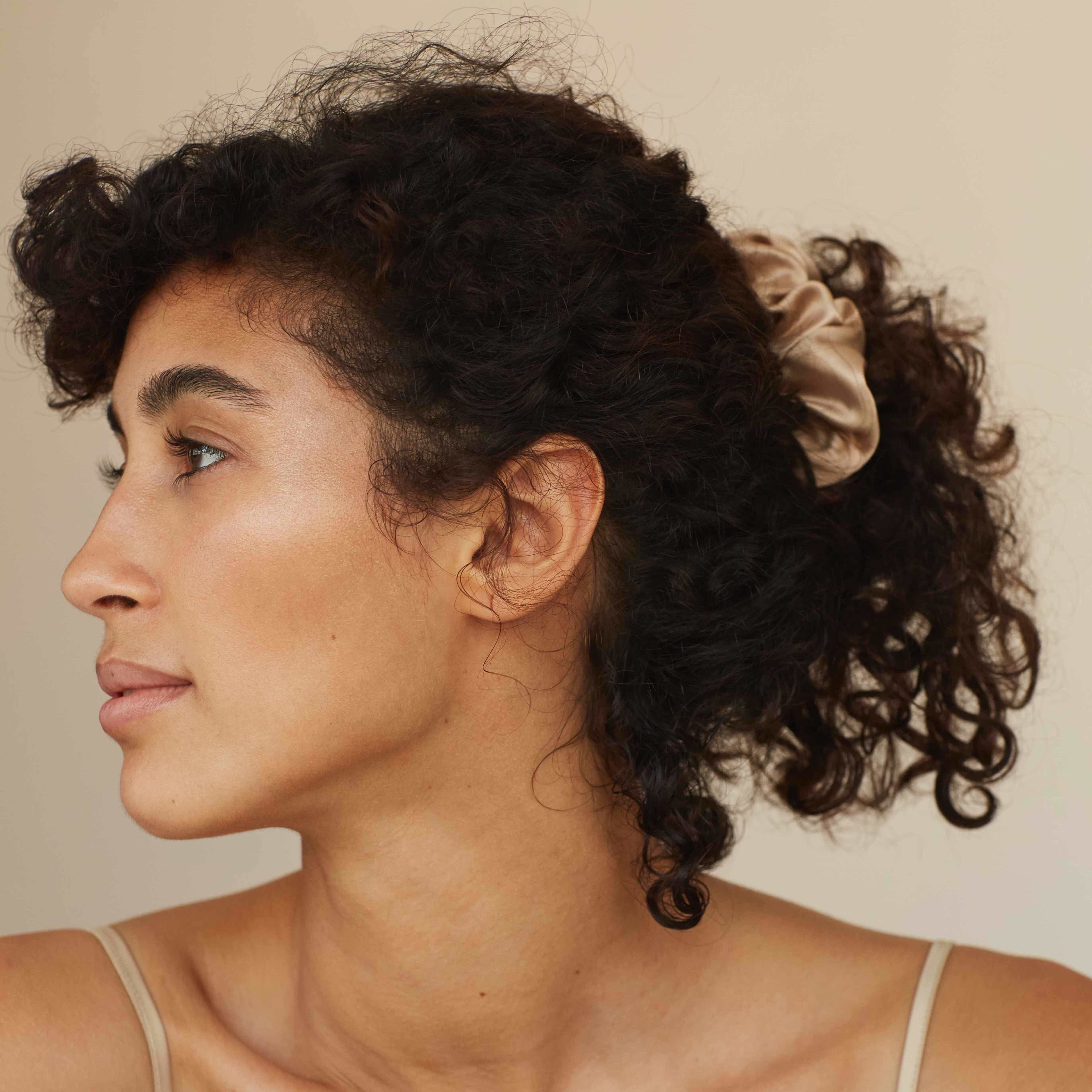 Beige silk scrunchie by Dariia Day styled in curly hair, showcasing its smooth texture