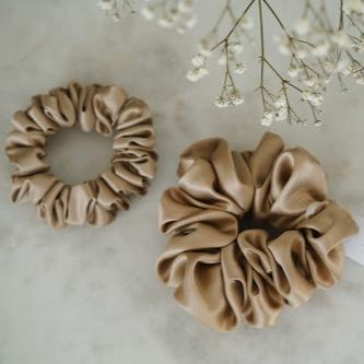 Two beige silk scrunchies by Dariia Day displayed with flowers, showcasing luxury hair accessories