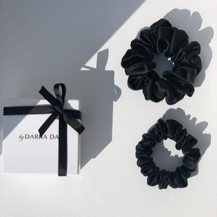 Two black silk scrunchies by Dariia Day displayed next to a white gift box with black ribbon, perfect for gifting