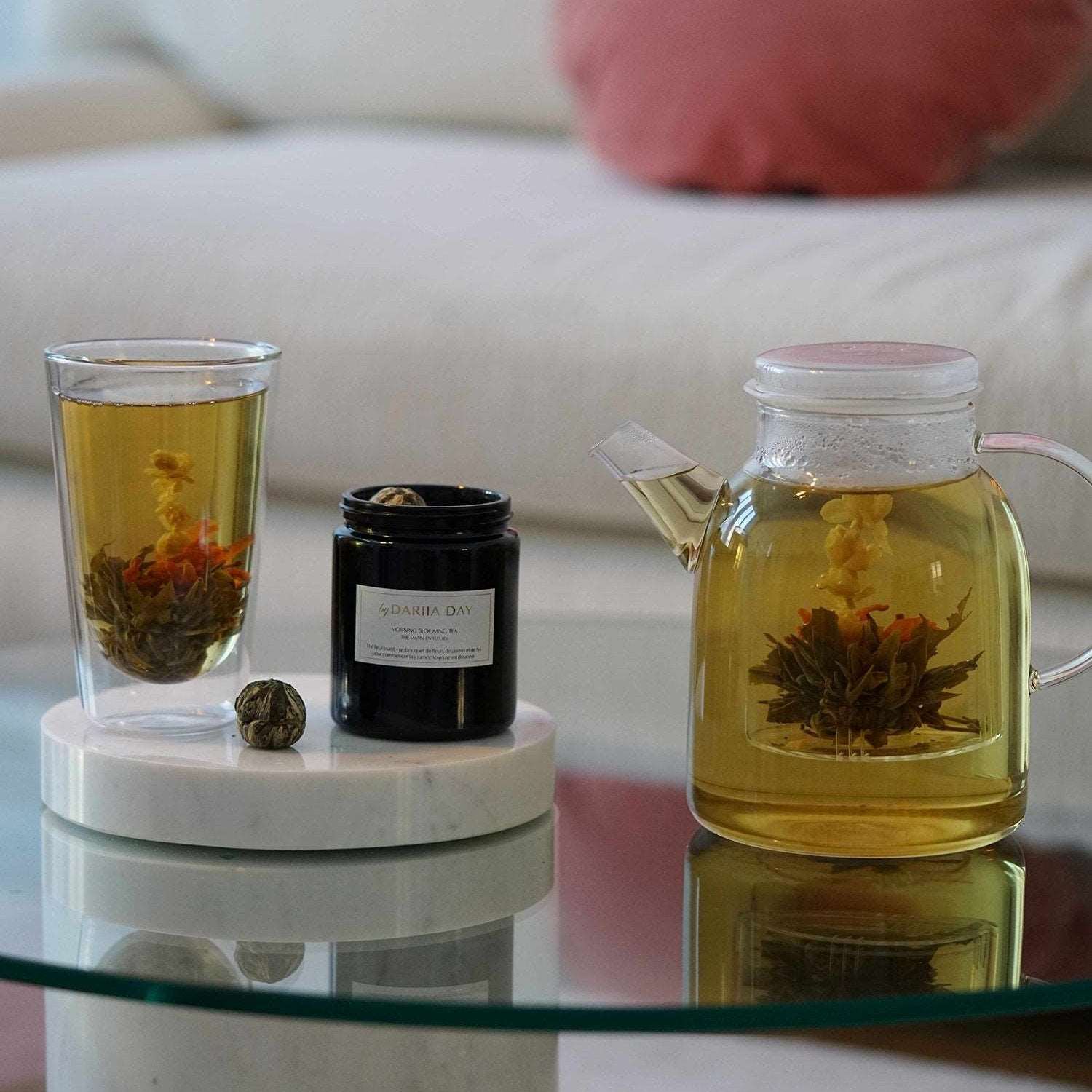 Dariia Day Morning Blooming Tea in a glass with blooming flowers, accompanied by a Silky Body Candle on a marble coaster.