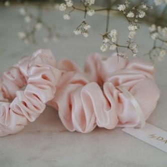 Two blush pink silk scrunchies by Dariia Day, displayed with delicate flowers for a luxurious aesthetic