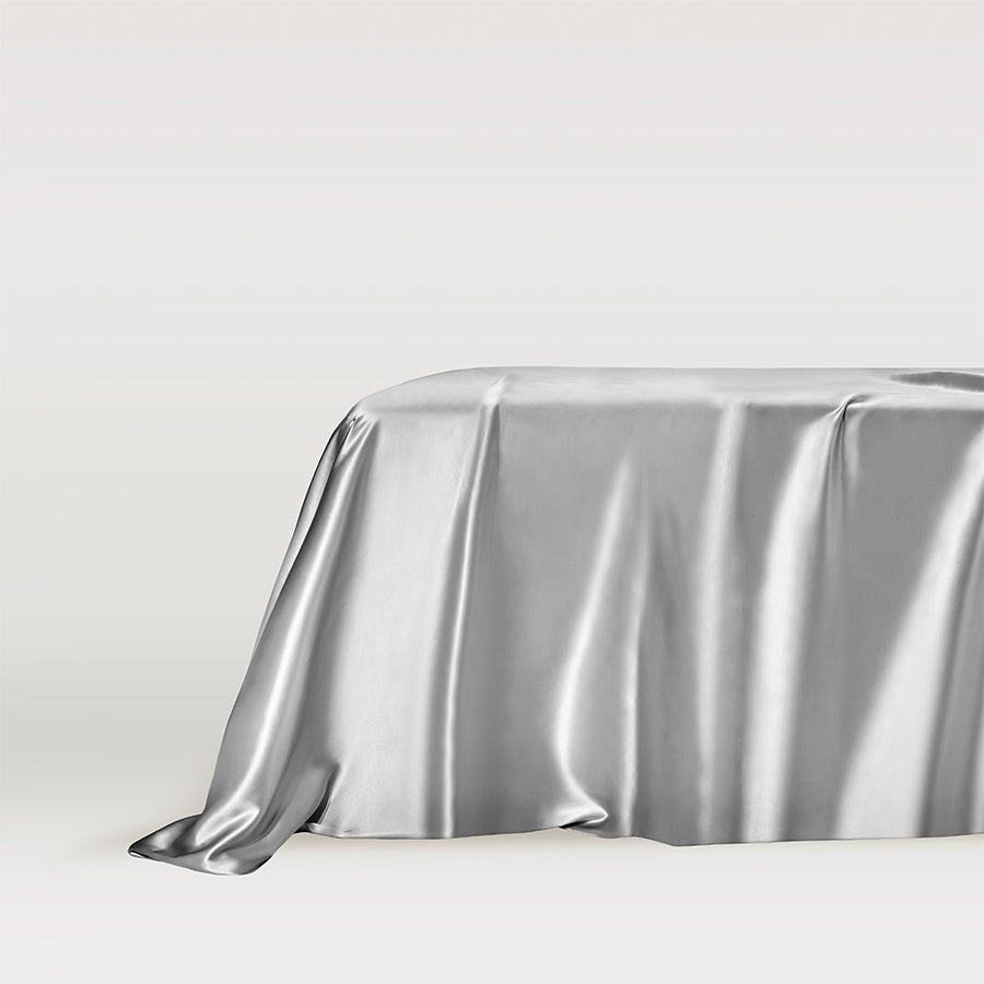 Grey Silver grey silk flat bed sheet draped elegantly on a bed by Dariia Day, showcasing smooth and luxurious texture.