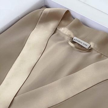 Close-up of a beige silk robe by Dariia Day, folded in a box with a focus on the smooth fabric and brand label.