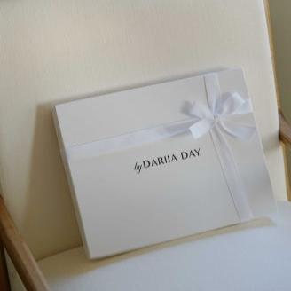 Dariia Day silk wedding gift box with ribbon placed on a cream-colored chair, offering a luxurious presentation.