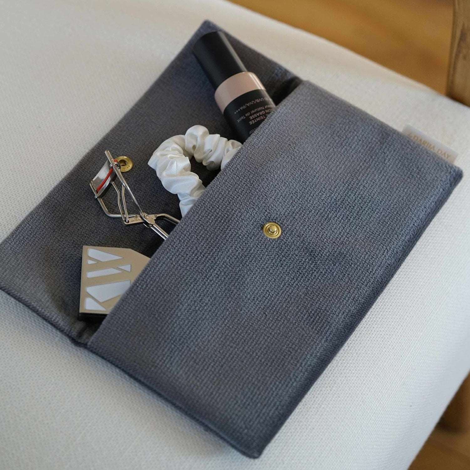 Dariia Day Moonstone Velvet Pouch filled with beauty essentials, including a scrunchie and makeup, displayed on a beige chair.