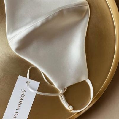 White Powder white silk face mask by Dariia Day displayed elegantly on a gold tray, showcasing the luxurious fabric.